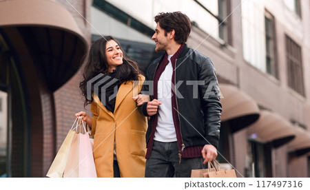 A man and woman are walking down a busy street, holding shopping bags in their hands. 117497316