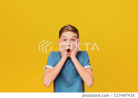 Surprised little boy. Shocked kid keeping mouth open and touching face, orange studio background Surprised little boy. Shocked kid keeping mouth open and touching face, orange studio background 117497438
