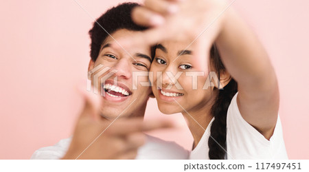 A cheerful young African American couple smiles and poses playfully with a bright pink background. They both wear white shirts and appear excited and happy, sharing a joyous moment together. A cheerful young African American couple smiles and poses playfully with a bright pink background. They both wear white shirts and appear excited and happy, sharing a joyous moment together. 117497451
