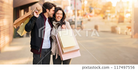 A couple walking down the street while holding shopping bags, enjoying a day out together. A couple walking down the street while holding shopping bags, enjoying a day out together. 117497556