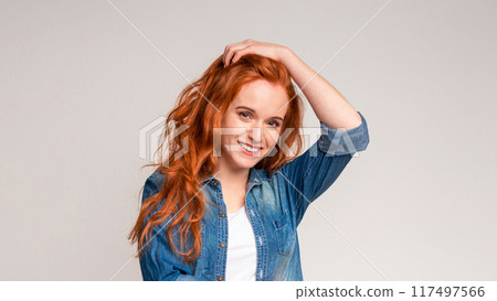 A woman with vibrant red hair is striking a pose for a picture. She is confidently displaying her unique features and style to the camera, touching head A woman with vibrant red hair is striking a pose for a picture. She is confidently displaying her unique features and style to the camera, touching head 117497566