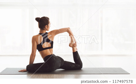A woman wearing a black sports bra top is seen performing yoga poses. Her body is engaged in various stretches, demonstrating flexibility and balance, focused and determined in her practice. 117497578