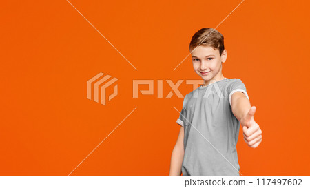 Like sign. Cute teen boy showing thumb up gesture, orange studio background 117497602