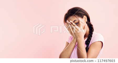 Shy African American girl covering her face with palms and peeking through fingers, pink background, panorama with copy space 117497603