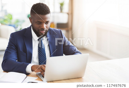 Young african businessman working in modern high tech office, typing on laptop, free space Young african businessman working in modern high tech office, typing on laptop, free space 117497676