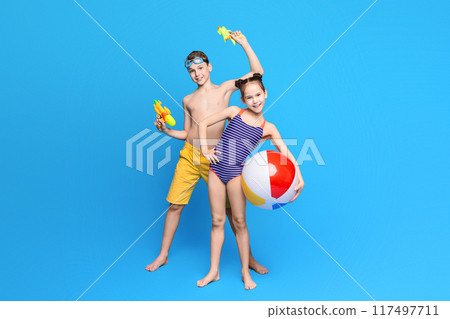 Happy summer holidays. Cheerful boy and girl playing with beach toys, blue studio background Happy summer holidays. Cheerful boy and girl playing with beach toys, blue studio background 117497711