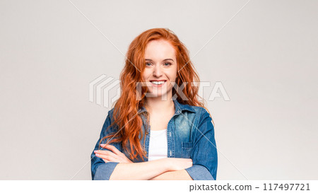 A red-haired woman is striking a pose for a photograph. She stands confidently, looking directly at the camera with a captivating gaze A red-haired woman is striking a pose for a photograph. She stands confidently, looking directly at the camera with a captivating gaze 117497721