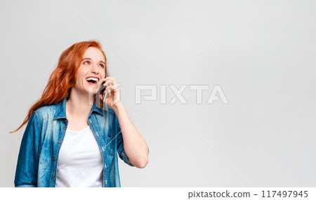 A woman with vibrant red hair is engaged in a phone conversation on her mobile device. She appears focused and animated as she communicates verbally through the phone, copy space A woman with vibrant red hair is engaged in a phone conversation on her mobile device. She appears focused and animated as she communicates verbally through the phone, copy space 117497945