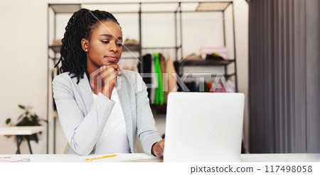Concentrated African American woman is seated at a desk, focused on the screen of her laptop. She appears engaged in the task at hand, possibly working or studying Concentrated African American woman is seated at a desk, focused on the screen of her laptop. She appears engaged in the task at hand, possibly working or studying 117498058
