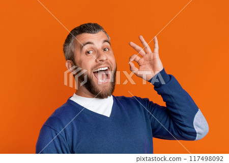 A man is playfully contorting his face with his hands, shaping it into a goofy and humorous expression. He seems to be engaging in a lighthearted and comical moment. 117498092