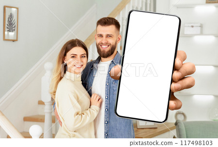 A man and a woman standing together, holding up a cell phone in their hands. 117498103