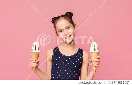 Enjoy it. Cheerful girl offering two ice cream cones, smiling on camera, pink studio background Enjoy it. Cheerful girl offering two ice cream cones, smiling on camera, pink studio background 117498107