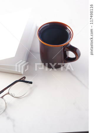 Image of a book, glasses and a coffee mug on a white table, enjoying reading while drinking coffee 117498116