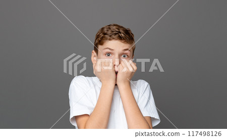 Teenager boy biting his nails in a pose reflecting anxiety and fear, isolated on a grey backdrop, capturing a common youngster behavior Teenager boy biting his nails in a pose reflecting anxiety and fear, isolated on a grey backdrop, capturing a common youngster behavior 117498126