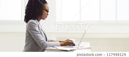Black businesswoman is concentrating on office work at her desk. The environment is sleek and modern, highlighting her dedication and focus on the task at hand. Black businesswoman is concentrating on office work at her desk. The environment is sleek and modern, highlighting her dedication and focus on the task at hand. 117498129