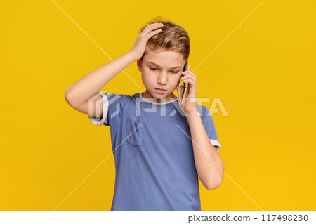 Fear and upset for mistake. Teenage boy talking on phone, holding hand on head in stress, orange studio background Fear and upset for mistake. Teenage boy talking on phone, holding hand on head in stress, orange studio background 117498230