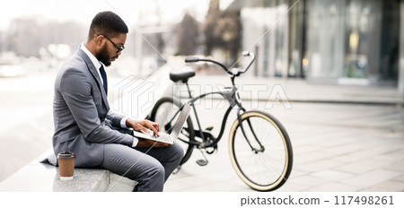 Black guy entrepreneur wearing suit and eyeglasses using laptop during coffee break, sitting at urban area, copy space, web-banner Black guy entrepreneur wearing suit and eyeglasses using laptop during coffee break, sitting at urban area, copy space, web-banner 117498261