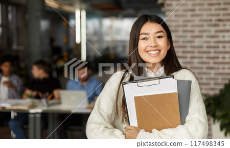 Happy girl in modern library smiling to camera, classmates studying on background in high school university 117498345