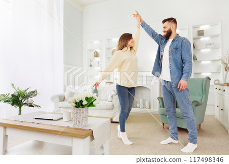 A man and a woman are standing in a modern living room, looking towards the camera. 117498346