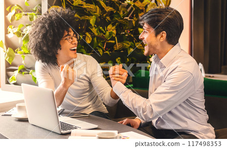 We did it. Excited partners celebrating success of their small business project, working on laptop in cafe, empty space. 117498353