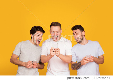 Surprised friends holding mobile phones, reading good news over orange background 117498357