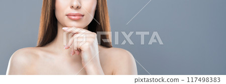 A young woman with long straight hair is posing in front of a grey backdrop. She is looking directly at the camera while touching her chin with her right hand, cropped, copy space A young woman with long straight hair is posing in front of a grey backdrop. She is looking directly at the camera while touching her chin with her right hand, cropped, copy space 117498383