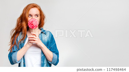 A woman is holding a colorful lollipop in her hands. She is looking at it with a smile on her face, enjoying the sweet treat, copy space 117498464