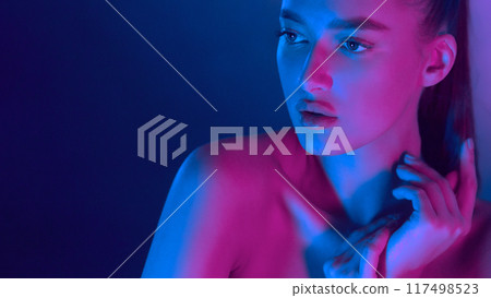 A woman gazes thoughtfully into the distance, bathed in vibrant neon lights that blend blue and pink hues, creating a striking and contemplative scene. A woman gazes thoughtfully into the distance, bathed in vibrant neon lights that blend blue and pink hues, creating a striking and contemplative scene. 117498523