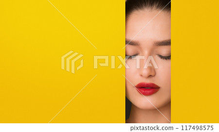 Sensual woman face is partially visible as she peeks out from a bright yellow background. Her eyes are looking directly at the viewer, conveying a sense of curiosity and intrigue. Sensual woman face is partially visible as she peeks out from a bright yellow background. Her eyes are looking directly at the viewer, conveying a sense of curiosity and intrigue. 117498575