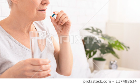 Cropped of senior woman as she prepares to take her medication, holding a pill between her fingers while also grasping a clear glass of water, copy space Cropped of senior woman as she prepares to take her medication, holding a pill between her fingers while also grasping a clear glass of water, copy space 117498634