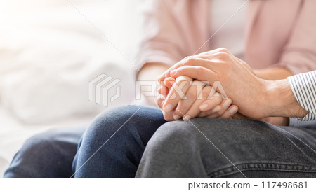 A man and a woman are seated on a couch, holding hands. They show affection and closeness in their body language as they enjoy each others company, cropped A man and a woman are seated on a couch, holding hands. They show affection and closeness in their body language as they enjoy each others company, cropped 117498681