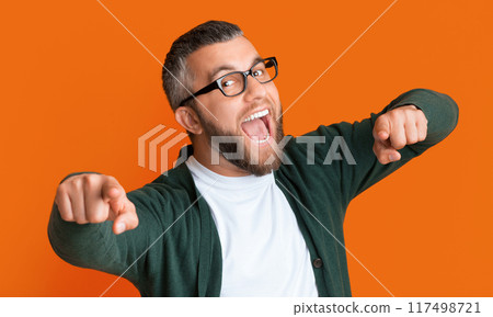 A man with glasses and a green cardigan stands in the foreground. He is looking and pointing directly at the camera A man with glasses and a green cardigan stands in the foreground. He is looking and pointing directly at the camera 117498721