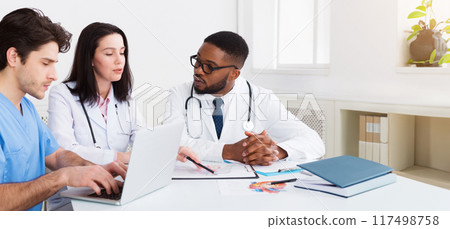 Young medical team discussing reports, using laptop in meeting room 117498758