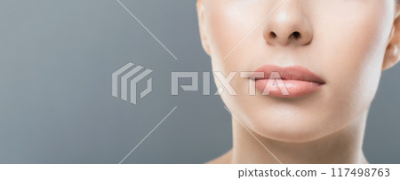 A woman face is shown in a close-up, highlighting her clear, smooth skin and neutral lip color. The background is a plain gray, cropped, copy space 117498763