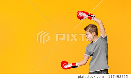 Transitional age problems. Furious teenager in boxing gloves screaming and attacking at empty space, orange panorama background Transitional age problems. Furious teenager in boxing gloves screaming and attacking at empty space, orange panorama background 117498835