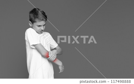 The youngster's face contorted in pain as he touches his elbow, suggesting an injury isolated on grey 117498888