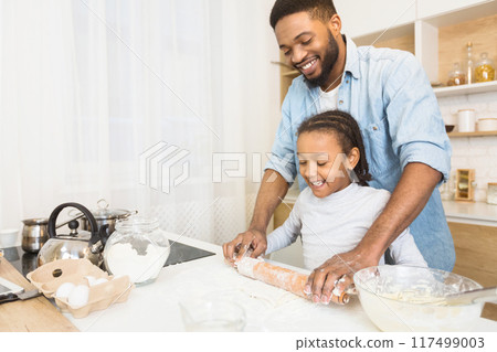 Smiling Black Man And His Daughter Rolling Dough Together At Kitchen, copy space Smiling Black Man And His Daughter Rolling Dough Together At Kitchen, copy space 117499003