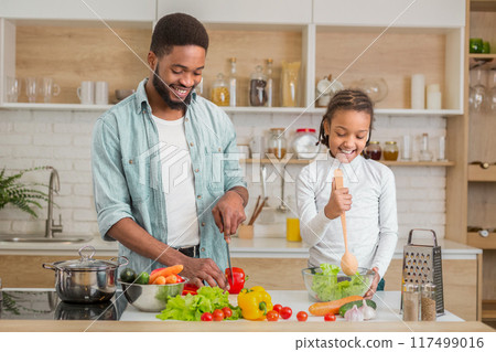 Black father and his daughter give thumbs up while cooking together in the kitchen, enjoying family time and embracing fatherhood Black father and his daughter give thumbs up while cooking together in the kitchen, enjoying family time and embracing fatherhood 117499016