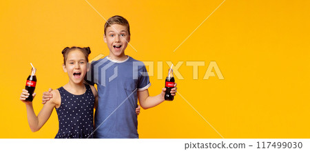 KHARKIV, UKRAINE - April 03. 2019: Happy children drinking Coca-Cola Classic with straws on orange background. The drink is produced and manufactured by The Coca-Cola Company 117499030