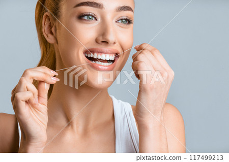 Tooth care. Young woman using dental floss over grey studio background Tooth care. Young woman using dental floss over grey studio background 117499213
