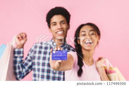 Happy teenage couple showing credit card and holding shopping bags, pink background 117499300