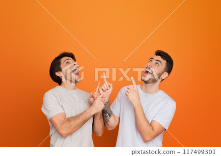 The two european guys laugh and point up, possibly sharing an inside joke or a fun suggestion among friends 117499301