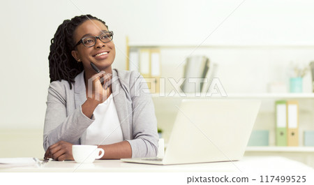 Dreamy African American businesswoman sitting at her office, working on laptop, looking at copy space, panorama 117499525