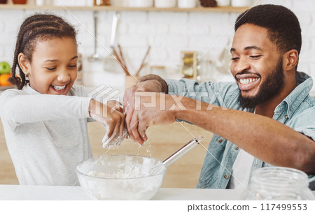 Happy black dad and daughter adding flour into dough bowl, making pastry together, kitchen interior 117499553