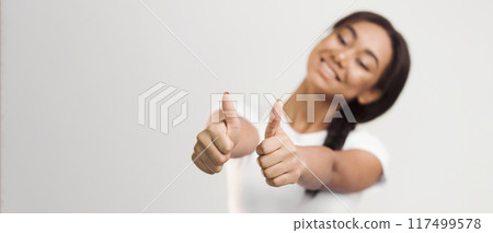 African American girl is shown in the photograph with her arm raised, giving a thumbs up gesture on a plain white background. She is smiling and appears to be expressing approval or agreement. African American girl is shown in the photograph with her arm raised, giving a thumbs up gesture on a plain white background. She is smiling and appears to be expressing approval or agreement. 117499578