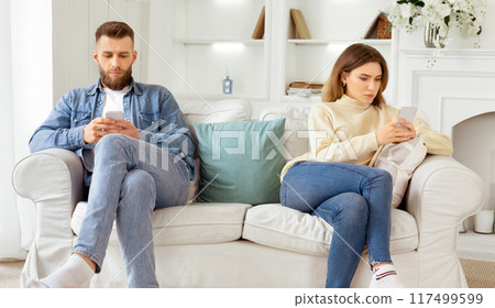 Family quarrel. Couple Staring At Their Own Smartphones, Sitting On Different Sides Of Couch Family quarrel. Couple Staring At Their Own Smartphones, Sitting On Different Sides Of Couch 117499599