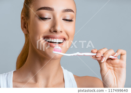 Healthy teeth. Happy girl brushing her perfect teeth, holding toothbruch, grey background Healthy teeth. Happy girl brushing her perfect teeth, holding toothbruch, grey background 117499640