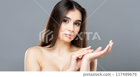 A young woman with long brown hair poses gracefully against a gray background. She has a serene expression and is holding her hands delicately. 117499678