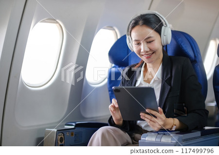 A woman is sitting on an airplane with a tablet in front of her A woman is sitting on an airplane with a tablet in front of her 117499796