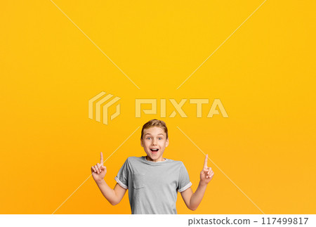 It's great. Amazed smiling teen boy pointing two fingers up at empty space, orange studio background It's great. Amazed smiling teen boy pointing two fingers up at empty space, orange studio background 117499817